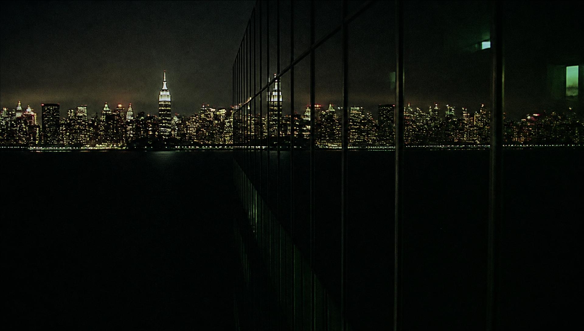 Manhattan at night reflected across the dark glass facade of a skyscraper
